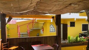A yellow building with a staircase, wooden furniture, and a covered outdoor seating area. - Pousada Dona Elena (Penha)