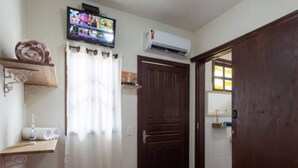 A bedroom with a bed, a television mounted on the wall, an air conditioning unit, a wooden door, and a window with curtains. - Pousada Dona Elena (Penha)
