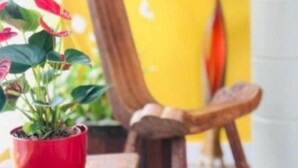 A wooden table with a carved design, a red potted plant, and a wooden chair in a room with yellow walls. - Pousada Dona Elena (Penha)