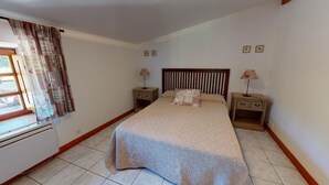 Un dormitorio con una cama, dos mesitas de noche, una ventana con cortinas y un radiador.