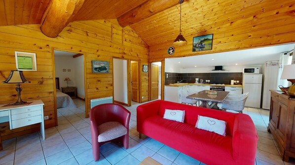 A cozy cabin interior with a red sofa, wooden walls, a dining area, and a kitchen.