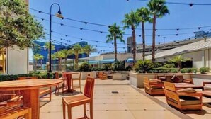 An outdoor patio area with round tables and wooden chairs, surrounded by palm trees and plants. -  Strip View/ MGM Signature Studio ★ No resort fees (Las Vegas)