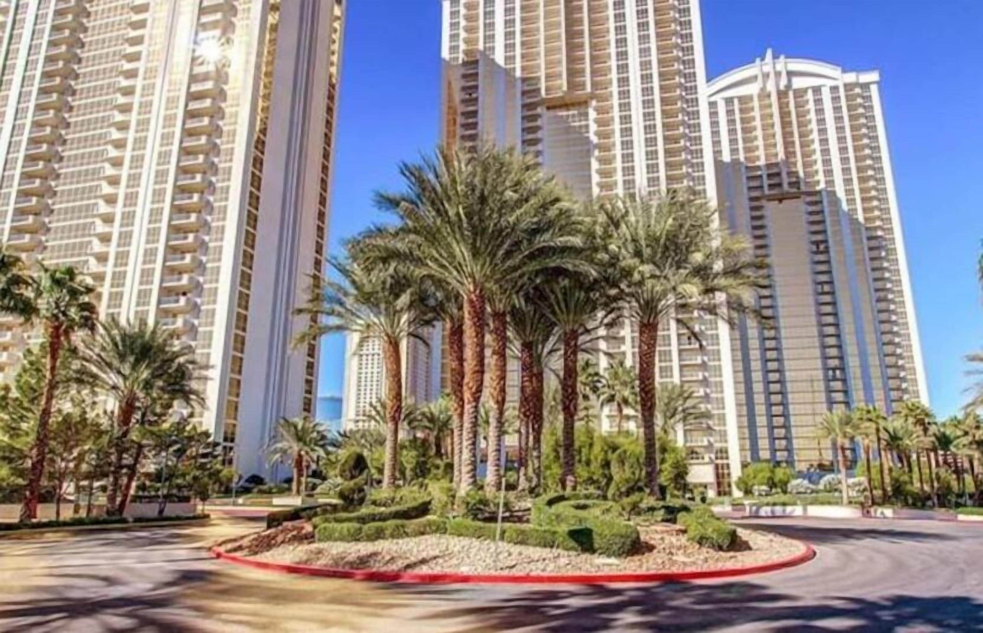 A high-rise residential building complex with multiple balconies, surrounded by palm trees and well-maintained landscaping.