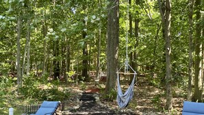 A forested area with a hammock, two lounge chairs, and a fire pit. - Private Home in Poconos -Country Club-New Renovated heated Pool, Beach, & more  (Tobyhanna)