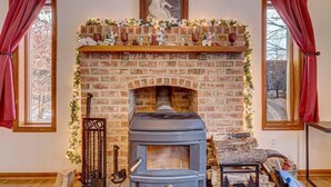 A cozy room with a brick fireplace, a wood-burning stove, and a mantel decorated with flowers and candles. - Private Home in Poconos -Country Club-New Renovated heated Pool, Beach, & more  (Tobyhanna)