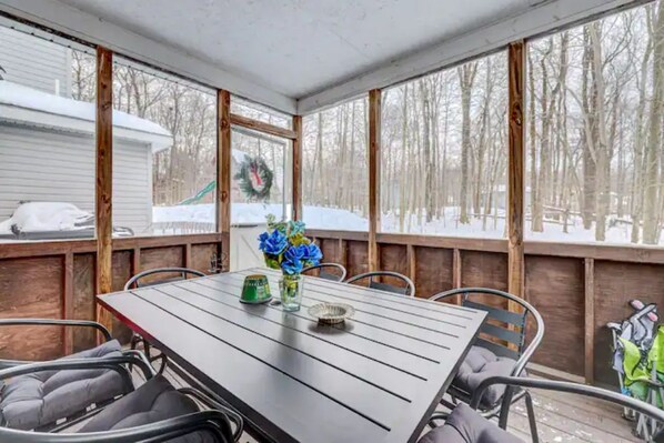 A covered patio with a table and chairs, a wreath on the window, and a snowy landscape outside.