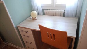 Una habitación pequeña y bien iluminada con un escritorio de madera clara, una silla y un radiador.
