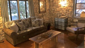 A cozy living room with a stone wall, a sofa, a wooden coffee table, and a stone fireplace. - 1930's Stone Cottage with spectacular views! (Lake Montezuma)