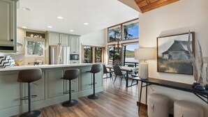 A modern kitchen with a bar area, wooden flooring, and large windows.