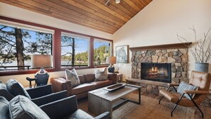 A cozy living room with a stone fireplace, leather furniture, and large windows.