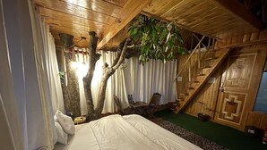 Un dormitorio con una cama grande, paredes de madera, una escalera y una planta colgante.