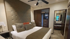 A modern bedroom with a large bed, a ceiling fan, a built-in wardrobe, and a bathroom with a mirror and sink.