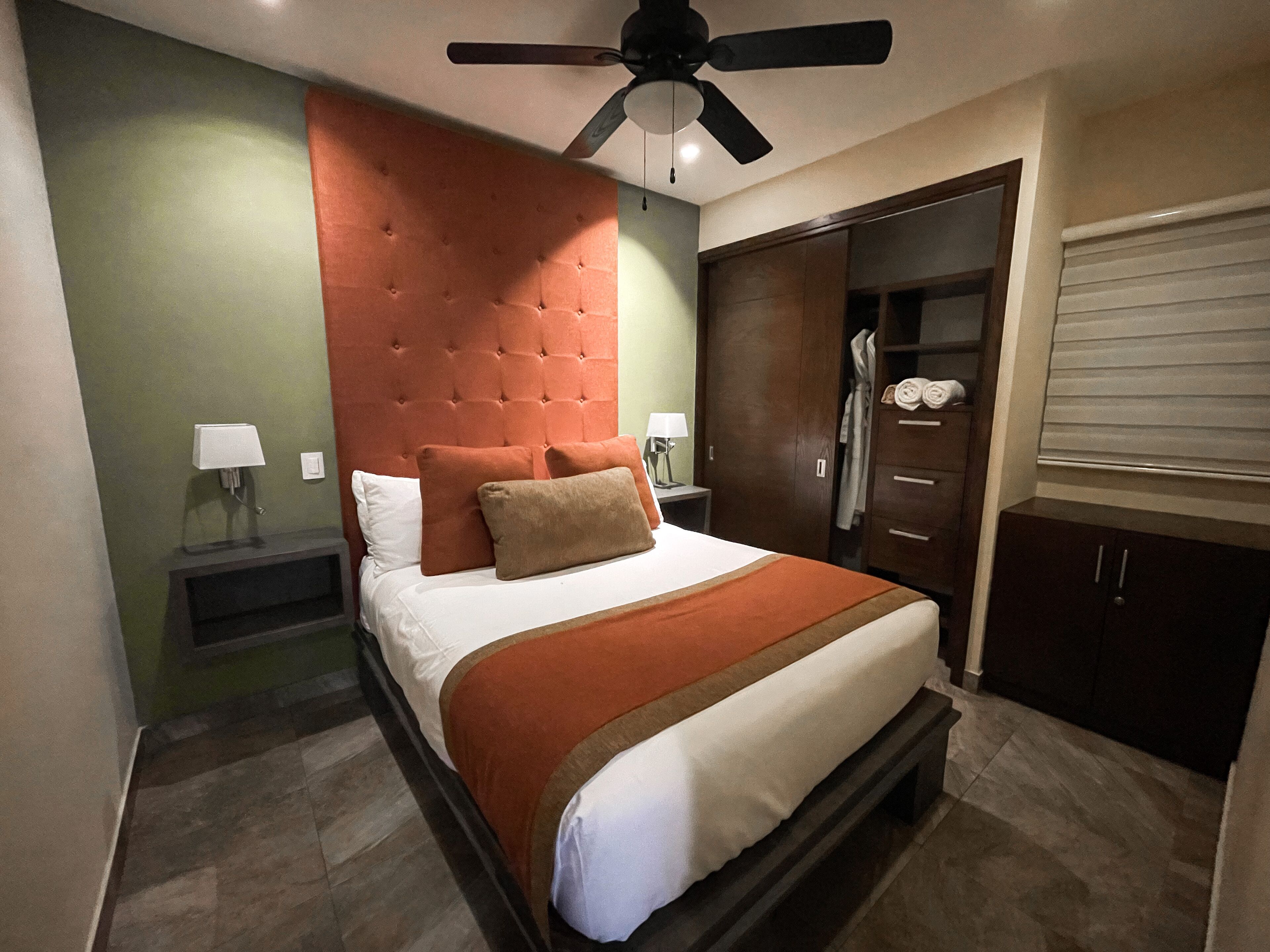 Una habitación de hotel con cama, ventilador de techo, armario y mesita de noche con lámpara.