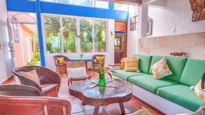 Una sala de estar acogedora con un sofá verde, sillas de mimbre y una mesita de centro.