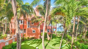 Un edificio de varios pisos con fachada roja, rodeado de abundante vegetación y palmeras.