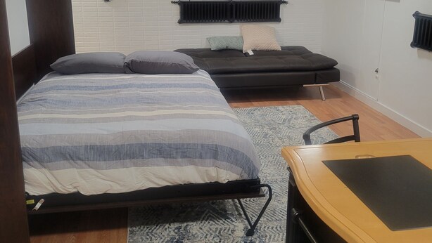 A bedroom with a bed, a sofa, a small table, and a radiator. - Home Away Studio Basement Apartment w/Hideabed (Ogden)
