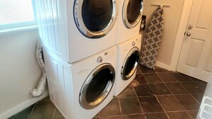 A laundry room with four stacked front-loading washing machines, a vent pipe, a patterned towel, and a door. - Home Away Studio Basement Apartment w/Hideabed (Ogden)
