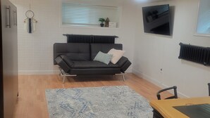 A living room with a black sofa, a blue patterned rug, and a wooden floor. - Home Away Studio Basement Apartment w/Hideabed (Ogden)