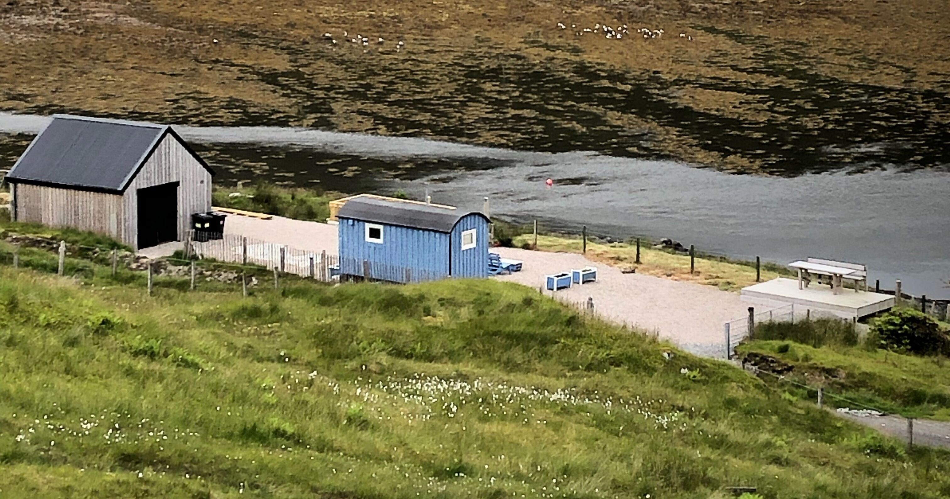A small coastal building with a dock, a blue shed, and a bench by the water.