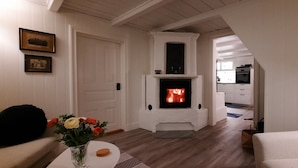 A living room with a fireplace, a sofa, a coffee table with flowers, and a kitchen in the background. - Swedish idyll - dreamlike secluded location - close to the lake - sauna - pool table (Nybro)