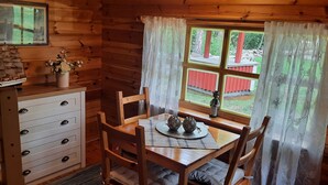 A wooden cabin interior with a dining table, chairs, a dresser with drawers, a ship model, and a window with curtains. - Swedish idyll - dreamlike secluded location - close to the lake - sauna - pool table (Nybro)