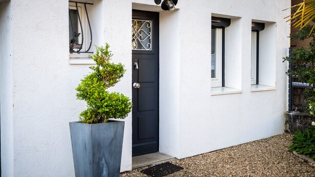 Un bâtiment blanc avec une porte noire, deux fenêtres et un petit balcon.