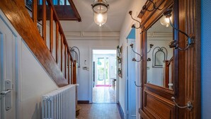 Un couloir avec un escalier en bois, un radiateur et une porte dotée d’un miroir.
