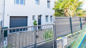 Un bâtiment blanc à deux étages, doté d’un garage, d’un petit jardin et d’une clôture en métal.