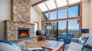 A living room with a stone fireplace, a television, and a large window offering a view of the outdoors. - Stunning views of the lake, private balcony & gorgeous fireplace - Spacious Marina Cay Getaway (Bigfork)