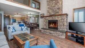 A spacious living area with a stone fireplace, a flat-screen TV, and a dining area in the background. - Stunning views of the lake, private balcony & gorgeous fireplace - Spacious Marina Cay Getaway (Bigfork)