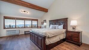 A bedroom with a large bed, wooden floor, a window with blinds, a bedside table with a lamp, and a heater on the wall. - Stunning views of the lake, private balcony & gorgeous fireplace - Spacious Marina Cay Getaway (Bigfork)