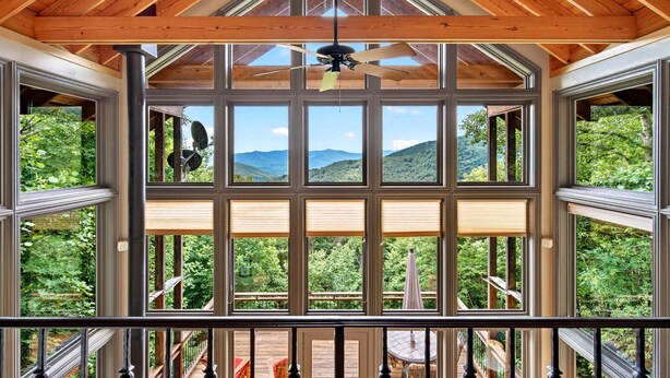 A wooden ceiling with a ceiling fan, large windows with blinds, and a view of a deck and mountains. - High Haven | Breathtaking Mountain Views! (Black Mountain)