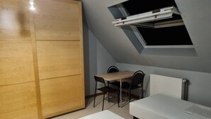 Ein Zimmer mit einem Holzschrank, einem Schreibtisch mit zwei Stühlen, einem Bett und einem Dachfenster.