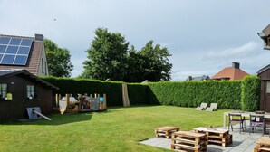 Ein Garten mit einem Holzschuppen, einer Solaranlage, einem Holzzaun und einer Terrasse mit Holzmöbeln.