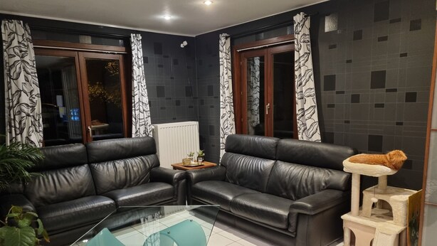 Ein modernes Wohnzimmer mit zwei schwarzen Ledersofas, einem Glastisch und einer Katzenkralle.