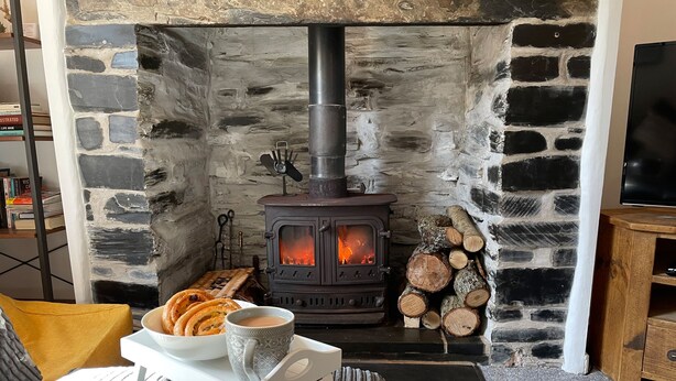 Una habitación acogedora con chimenea de piedra, una bandeja con pasteles y una taza, y un televisor sobre un soporte de madera.