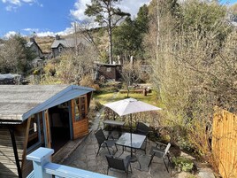 A patio area with a table and chairs, surrounded by a wooden fence and dense shrubbery.