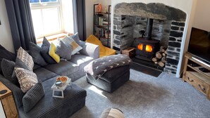 Una sala de estar acogedora con chimenea de piedra, un conjunto de sofás, un televisor y una estantería.