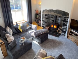 A cozy living room with a stone fireplace, a sofa set, a television, and a bookshelf.