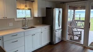 Una cocina moderna con armarios blancos, un refrigerador de acero inoxidable y un ventanal con vistas a una terraza.