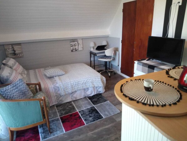 A small, cozy bedroom with a bed, a desk, a chair, and a television.