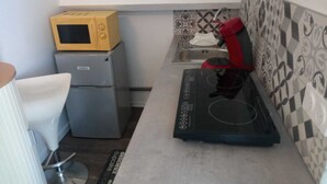 Een kleine keuken met een magnetron, een kleine koelkast, een rode waterkoker en een zwarte inductiekookplaat.