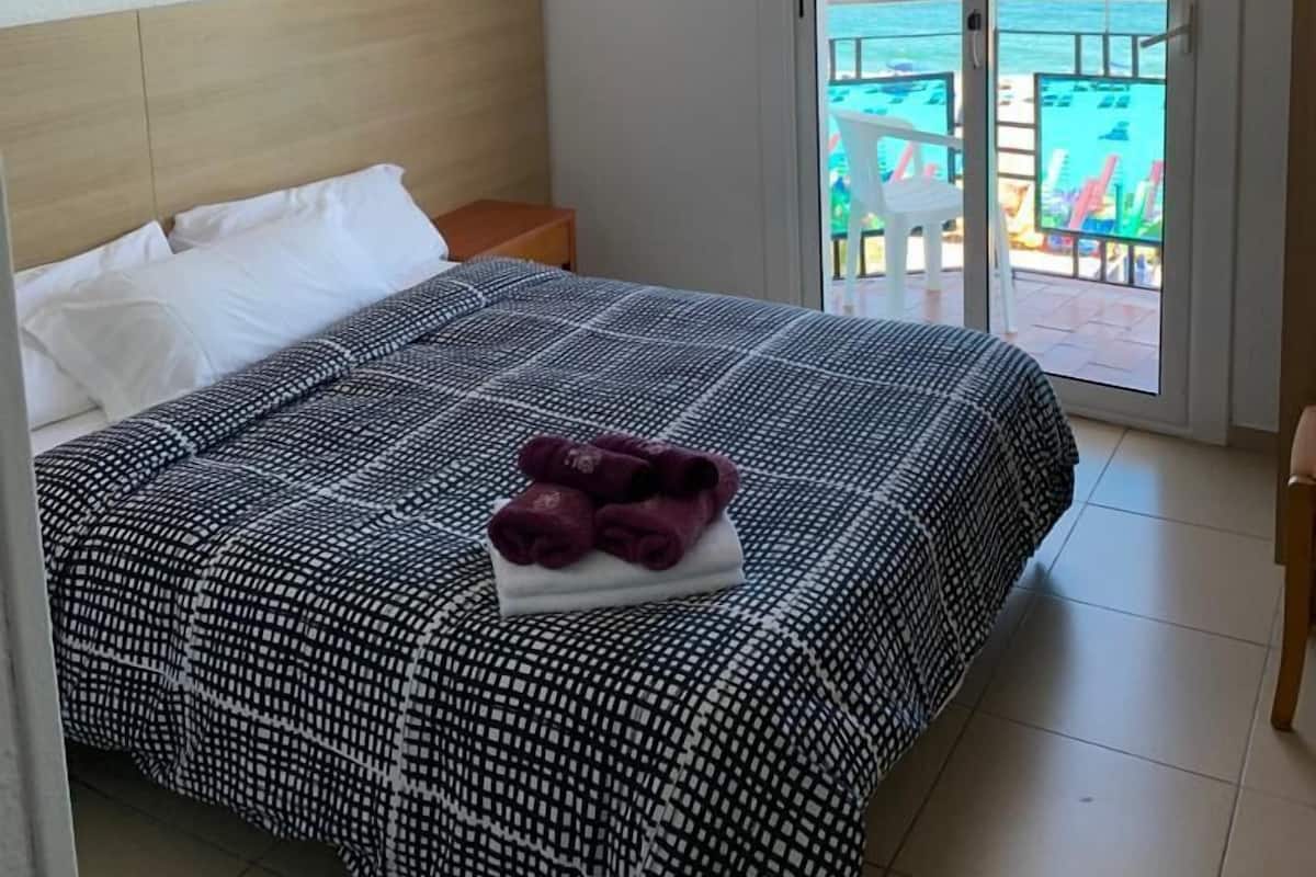 A bedroom with a bed, a nightstand, and a view of the ocean through a sliding glass door.