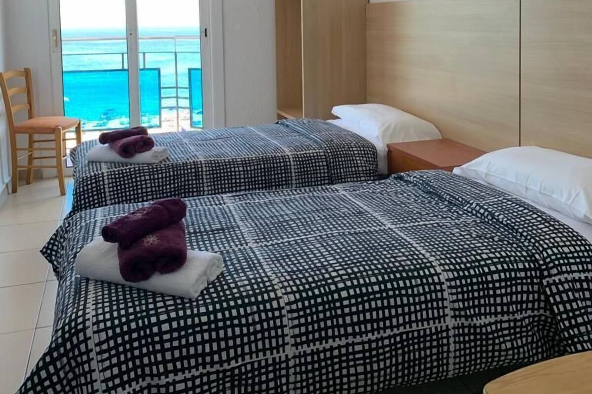 A hotel room with two beds, a wooden wardrobe, a small table, and a chair.