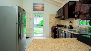 A kitchen with granite countertops, a stainless steel refrigerator, and a view of a garden through a glass door. - King Bed, Fully A/C, Pool, Gym, BBQ, Near beaches, Free Washer/Dryer (Ocho Rios)