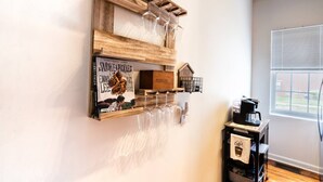 A wall-mounted wooden shelf with wine glasses, a book titled 'Smoke & Pickles' by Edward Lee, and a small model of a coffee house.