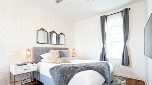 A bedroom with a bed, bedside tables, a mirror, a ceiling fan, and a window with curtains.