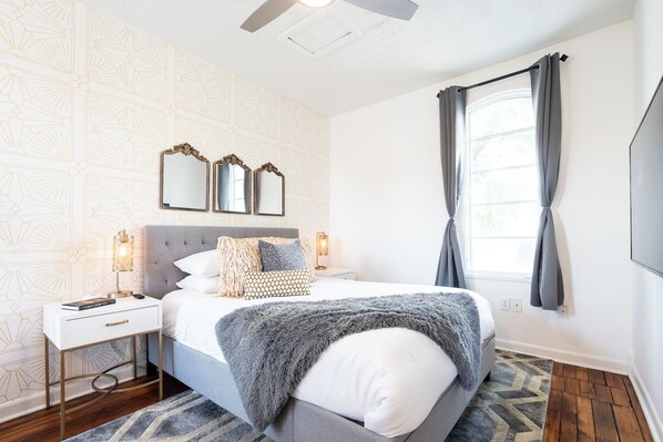 A bedroom with a bed, bedside tables, a mirror, a ceiling fan, and a window with curtains.