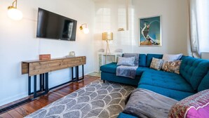 A modern living room with a blue sofa, a wooden console table, a flat-screen TV, and a painting on the wall.