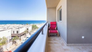 A balcony with a red chair, a view of the beach, and a building in the background. - Home2Book Bright Penthouse Médano, Terrace & Pool (El Medano)